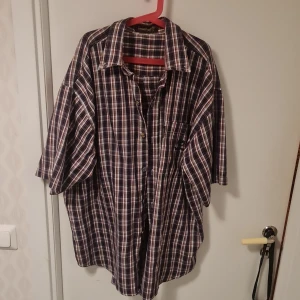 Rutig skjorta från Timberland - Säljer en klassisk rutig skjorta från Timberland i blått, vitt och rött. Skjortan har en avslappnad passform med korta ärmar och knappar framtill. Perfekt för en casual look.