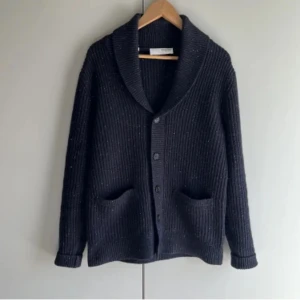 Svart ribbad kofta med knappar - Säljer en stilren svart ribbad kofta med knappar framtill. Koftan har en klassisk design med långa ärmar och två fickor. Perfekt för en avslappnad look.