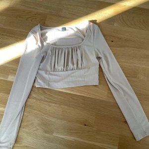 Beige ribbad topp från Shein - Säljer en beige ribbad topp från Shein med långa ärmar och en snygg rynkad detalj framtill. Perfekt för en stilren look. Toppen är i storlek S och har en croppad passform.