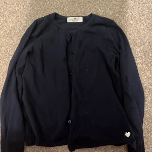 Mörkblå kofta från H&M - Säljer en stilren mörkblå kofta från H&M med knappar framtill. Koftan har långa ärmar och en söt hjärtdetalj vid nederkanten. Skriv först om ni skulle vilja köpa!💕