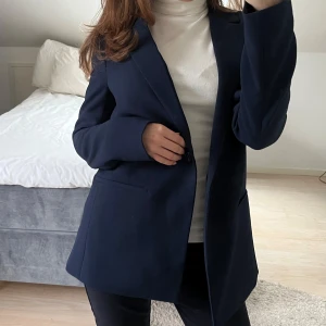 Mörkblå kavaj - Snygg mörkblå kavaj med en klassisk design. Kavajen har en enkelknäppning och två fickor som detalj. Knappast använd och köpt för ca 1200 kr. Passar en storlek S
