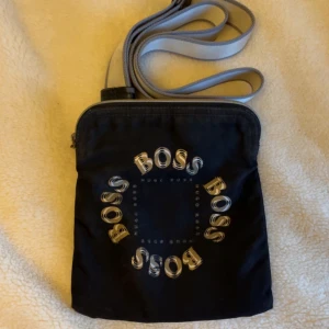 Svart axelväska från Boss - säljer en jävligt limited edition Hugo boss väska lite sliten men har väldigt mycke kvar att ge, hör av er vid frågor