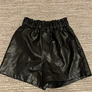 Svarta shorts i syntetmaterial - Snygga svarta  shorts i glansigt syntetmaterial med elastisk midja. Perfekta för en trendig look. Hör av mig er om ni har någon fråga!💕
