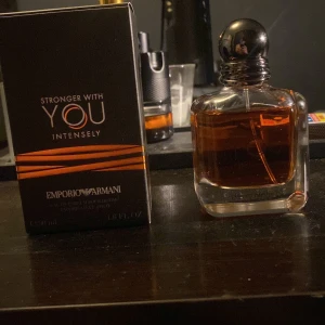 Emporio Armani Stronger With You Intensely - Säljer en flaska Emporio Armani Stronger With You Intensely. Parfymen kommer i en elegant glasflaska med en mörk bärnstensfärgad vätska och en stilren svart kork. Förpackningen är svart med orange detaljer och logotypen i silver. Perfekt för den som vill ha en intensiv och kraftfull doft.