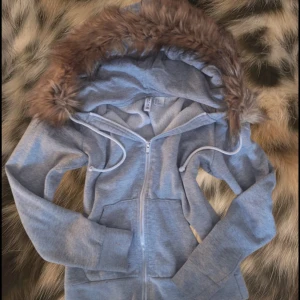 Grå hoodie med pälskant från H&M - Säljer en mysig grå hoodie från H&M med dragkedja och en fluffig pälskantad huva. Perfekt för kyliga dagar när du vill vara både varm och stilren. Hoodien har långa ärmar och en bekväm passform. Meddela bara om du har några frågor!!☺️😋