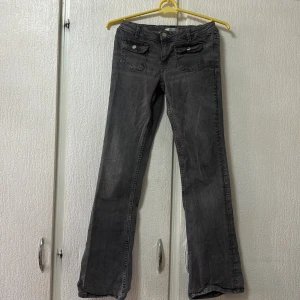 Grå jeansbyxor med bootcut - Snygga grå jeansbyxor med bootcut-stil. Byxorna har klassiska fem fickor och knappar i silverfärg. Perfekta för en avslappnad look.