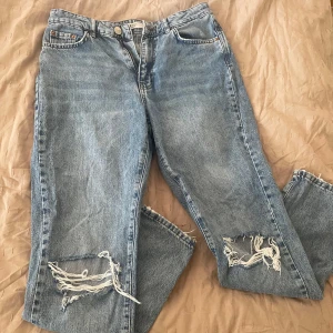 Blå jeans med slitningar från Gina Jeans - Snygga blå jeans från Gina  Jeans med slitningar på knäna. Perfekta för en avslappnad stil.