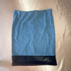 Grå kjol med svart detalj från Gina Tricot - Snygg grå kjol från Gina Tricot med en svart glansig kant längst ner. Perfekt för en stilren look. Kjolen är i en mjuk och bekväm kvalitet.