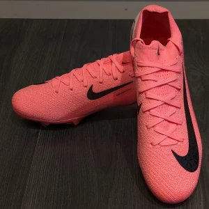 Rosa Nike Mercurial fotbollsskor - Pris kan diskuteras! Snygga rosa Nike Mercurial fotbollsskor med svart swoosh och text. Skorna har snörning och är designade för optimal prestanda på planen. Perfekta för den som vill sticka ut med stil och funktion.