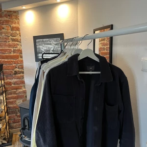 Mörkblå manchester overshirt från H&M - Säljer en stilren mörkblå overshirt från H&M i mjukt manchestertyg. Perfekt för lager-på-lager och har en klassisk krage med knappar framtill. Passar bra till både vardag och mer uppklädda tillfällen. Använd, små missfärgningar exempelvis armbåge.