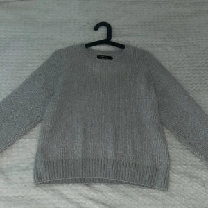 Grå stickad tröja från FB Sister - Säljer en mysig grå stickad tröja från FB Sister. Tröjan har en klassisk rund hals och långa ärmar med ribbade muddar vid ärmslut och nederkant. Perfekt för kyliga dagar!