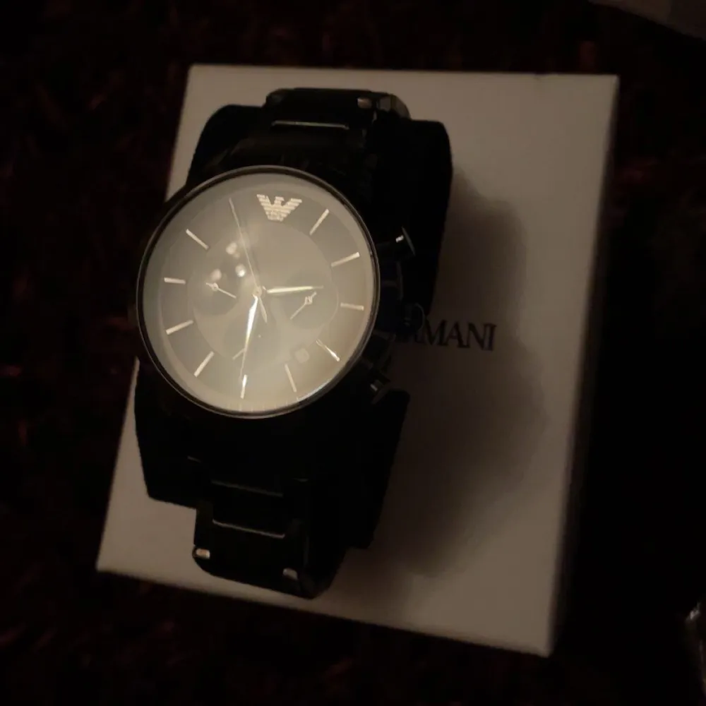 Snygg svart klocka från Emporio Armani med stilren design. Klockan har en svart urtavla med gulddetaljer och flera små urtavlor för extra funktionalitet. Perfekt accessoar för den stilmedvetna. man måste bara ställa in klockan i en butik.. Asusteet.