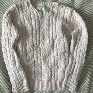 Ljusrosa/rosa stickad tröja - OBS MER ROSAAKTIG I VERKLIGHETEN! Mysig ljusrosa stickad tröja med kabelstickat mönster. Perfekt för kyliga dagar med sin klassiska design och rundade halsringning. Tröjan har långa ärmar och ribbade muddar vid ärmslut och nederkant. Pris går att diskuteras. Funkar för mig som är 157cm