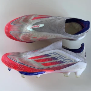 Adidas F50+ FG fotbollsskor - Säljer ett par Adidas F50+ FG fotbollsskor i strl 40. Det är ett par snygga och sköna skor i vitt, rött och blått. Skorna har en strömlinjeformad design med en lätt syntetisk överdel och FG-dobbar för optimalt grepp på gräsplaner. Perfekta för snabba spelare som vill ha en lätt och responsiv sko. De är i mycket bra skick 8/10, är använda några fåtal gånger. Ny pris på skorna var 3499kr. Kontakta mig om det finns några frågor!