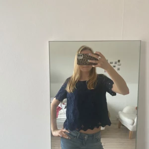 Mörkblå spetsblus - Säljer en mörkblå blus med spetsdetaljer. Blusen har korta ärmar och en lös passform, perfekt för en stilren look. Är i storlek M men passar S oxå!