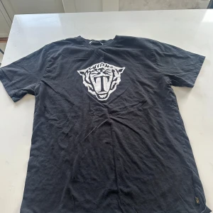 Svart t-shirt med tigertryck - Säljer en svart t-shirt med ett stort vitt tigertryck på framsidan. T-shirten har en normal passform och korta ärmar. Perfekt för en avslappnad stil.