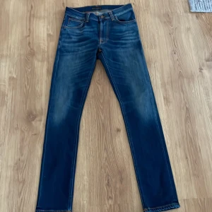 Blå jeans från Nudie Jeans - Snygga blå jeans från Nudie Jeans med klassisk femficksdesign och orange sömmar. De har en straight passform och är perfekta för en avslappnad stil.