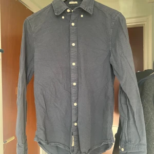 Mörkblå skjorta från East West - Säljer en stilren mörkblå skjorta från East West i slim fit. Skjortan har långa ärmar och knappar framtill. Perfekt för en snygg och avslappnad look.