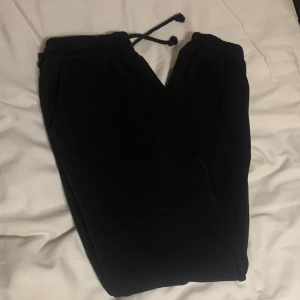 Svarta mjukisbyxor med snörning - Säljer ett par svarta mjukisbyxor med snörning i midjan. Perfekta för en avslappnad dag hemma eller på språng. Byxorna har elastisk midja och är gjorda i ett mjukt material för extra komfort.