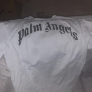 Turkos t-shirt från Palm Angels med nallemotiv - Säljer en turkos t-shirt från Palm Angels med ett unikt nallemotiv på framsidan. T-shirten har korta ärmar och är tillverkad i mjukt material. Perfekt för en avslappnad stil.