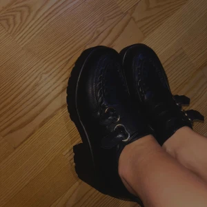 Svarta loafers med klack - Snygga svarta loafers i skinn med robust klack och dekorativa spännen. Perfekta för en stilren look med en touch av elegans. Passar bra till både jeans och klänning. Passar både en 38a och 39a!! Använd fåtal gånger.