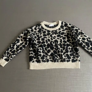 Leopardmönstrad stickad tröja - leopardmönstrad stickad tröja i beige och svart. Tröjan har långa ärmar och ribbade kanter vid hals, ärmslut och nederkant. 
