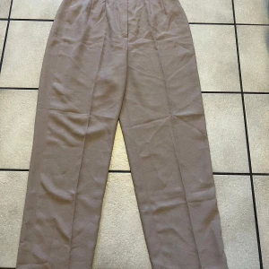 Beige kostymbyxor från Choice me - Snygga beige kostymbyxor från Choice me. De har en klassisk rak passform och är perfekta för en stilren look. Byxorna har en diskret dragkedja framtill och är tillverkade i ett lätt och bekvämt material. Midja 70 cm