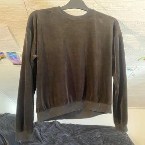 Svart sammetsliknande tröja från Kappahl - Mjuk och stilren svart tröja från Kappahl i sammetsliknande material. Tröjan har rund halsringning, långa ärmar och ribbade muddar vid ärmslut och nederkant. Perfekt för en enkel och snygg look.