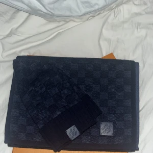 Mörkblå rutig halsduk och mössa från Louis Vuitton - Säljer en exklusiv mörkblå halsduk  från Louis Vuitton med matchande mössa. Halsduken har ett diskret rutigt mönster och är tillverkad i ett mjukt, stickat material. Perfekt accessoar för kyliga dagar och ger en lyxig känsla till din outfit Kvitto finns för mössan och lv halsduken är köpt från kaspersheat.