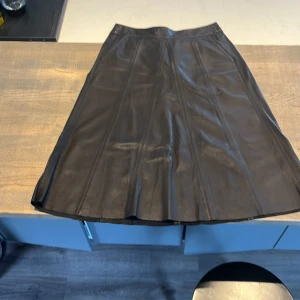 Svart skinnkjol från Mos Mosh - Säljer en svart långkjol i skinn från Mos Mosh. Kjolen har en snygg A-linjeform och dragkedja bak. Perfekt för dig som vill ha en stilren och edgy look.