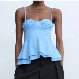 Blå volangtopp med smala axelband - Säljer en ljusblå topp med smala axelband och volang nertill. Helt ny, prislapp kvar!