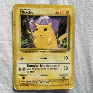 Pikachu Pokémonkort Base Set - Säljer ett klassiskt Pikachu-kort från Pokémon Base Set. Kortet har gul ram, motiv av Pikachu i en skogsmiljö och visar 40 HP. Kortet har attackerna Gnaw och Thunder Jolt. Perfekt för samlare eller Pokémon-fans!