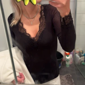 intimissimi tröja - Säljer en svart långärmad topp med djup v-ringning och fina spetsdetaljer längs halsringningen och ärmsluten, från intimissimi i storlek S.. Perfekt att styla med både jeans och kjol för en trendig look. 