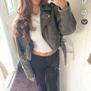 Svart skinnjacka med bälte - Säljer en grön  croppad skinnjacka med bälte och dragkedja. Jackan har klassisk bikerstil med bred krage och silvriga detaljer. Perfekt för dig som vill ha en edgy look till din outfit. Ord pris 900kr