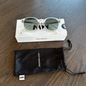 Transparenta solglasögon från MessyWeekend - Snygga solglasögon från MessyWeekend med transparent båge och runda, mörkgröna glas. Klassisk och stilren design som passar till många tillfällen. Levereras med originalfodral och ask. Glasögon storlek: 49:23