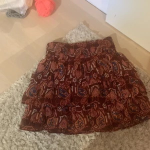 Mönstrad volangkjol från Lindex - Säljer en kort kjol från Lindex med paisleyinspirerat mönster i vinrött, blått och orange. Kjolen har flera volanger och resår i midjan för en bekväm passform. Perfekt för dig som gillar färg och mönster! Detta är själv min favorit men tyvärr är den för liten men hoppas någon annan får den till användning 