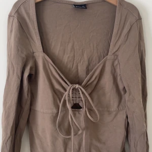 Beige långärmad topp med knyt - Säljer en brun/beige långärmad topp från Gina Tricot med djup v-ringning och knyt framtill. 