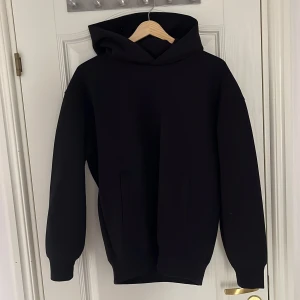 Svart hoodie - Uniqlo - En stilren svart hoodie med huva och långa ärmar. Perfekt för en avslappnad look och enkel att matcha med andra plagg. Tröjan är i M men den är liten i storleken (S/M)