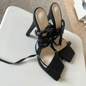 Svarta klackade sandaler med snörning - Säljer ett par svarta sandaler med hög klack och fyrkantig tå. Skorna har långa remmar som snöras runt vristen för en trendig look. Perfekta för dig som vill ha en stilren och modern sko med extra höjd. Är aldrig använda 💕