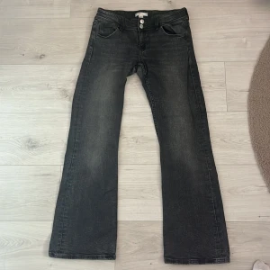Svarta bootcut jeans från Gina Tricot - Säljer ett par svarta bootcut jeans från Gina Tricot med två knappar i midjan och klassiska fickor fram och bak med knappar. Jeansen har en lätt tvättad look och är tillverkade i denim med snygg passform.