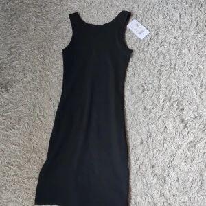 Svart klänning - Säljer en svart ribbad klänning från Stadium i storlek XS. Klänningen är ärmlös med rund halsringning och har en tight passform som framhäver figuren. Perfekt basplagg att styla på olika sätt. Prislappen är fortfarande kvar och den kostade från början 249. ☺️