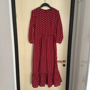 Röd prickig långklänning från SHEIN - Säljer en röd långklänning från SHEIN med vita prickar. Klänningen har lång ärm, rund halsringning, dragkedja i ryggen och volang nertill. Perfekt för dig som gillar retrostil och vill sticka ut med ett lekfullt mönster.