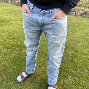 Levi's 502 ljusblå jeans - Säljer ett par klassiska ljusblå Levi's 502 jeans i premiumkvalitet. Jeansen har normal passform, raka ben och fem fickor. De är tillverkade i slitstarkt denim och har den ikoniska läderpatchen bak i midjan.