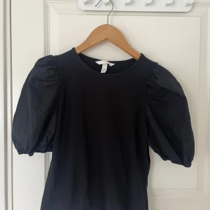 Svart topp med puffärmar - Säljer en svart topp med rund halsringning och trendiga puffärmar. Toppen har en enkel design men de voluminösa ärmarna ger en snygg statement-look. Perfekt att styla till både jeans och kjol.