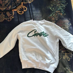 Vita shorts med grön logga från Corteiz - Vita shorts från corteiz med en stor grön logga längs ena benet. De har resår i midjan och snörning för extra komfort. Perfekta för en avslappnad stil under varma dagar. Och me en super fin corteiz sweatshirt 