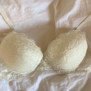 Vit spets-bh från Emilia - Säljer en elegant vit bh från Emilia med vacker spetsdetalj över hela kupan. Bh:n har tunna axelband och en feminin design som ger ett lyxigt intryck. Perfekt för dig som gillar romantiska underkläder.