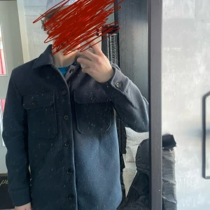 Mörkblå overshirt med knappar - Säljer en stilren mörkblå overshirt med klassisk krage och två stora bröstfickor med knappar. Jackan har långa ärmar och stängs med knappar framtill. Perfekt för lager-på-lager och enkel att matcha.