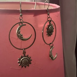 Silvriga örhängen med sol och måne - Unika örhängen i silverfärgad metall med stora ringar och detaljerade hängen av en måne och en sol.