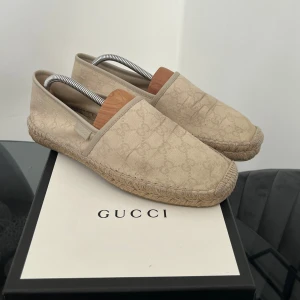 Beige espadrillos från Gucci - Säljer ett par snygga beige espadrillos från Gucci med diskret GG-mönster i tyget. Skorna har klassisk flätad sula och är perfekta för varmare dagar. Stilsäkra och lätta att matcha till olika outfits.