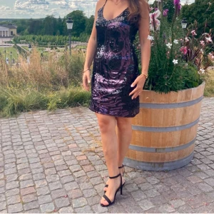 Lila paljettklänning med smala axelband - Säljer en glittrig lila paljettklänning med smala axelband och v-ringning. Klänningen är kort och har en figurnära passform som ger en festlig look. Perfekt för dig som vill sticka ut på nästa fest!